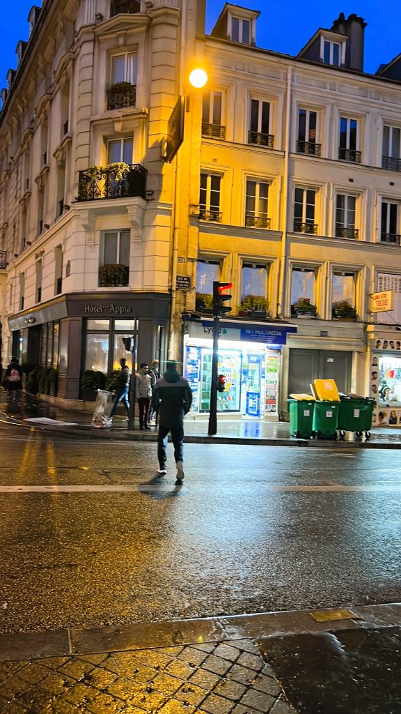 A night time street scene on a corner in Paris with the lights of a nearby store and people out walking