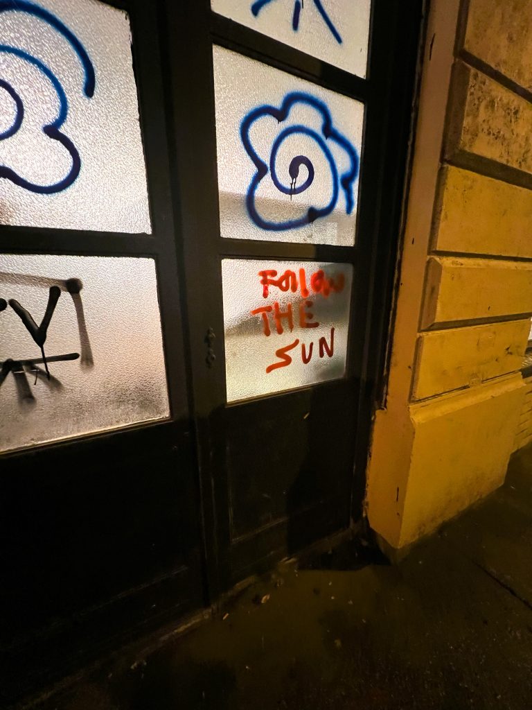 A photo of graffiti on windows of flowers and one pane says, "Follow the sun" in red paint