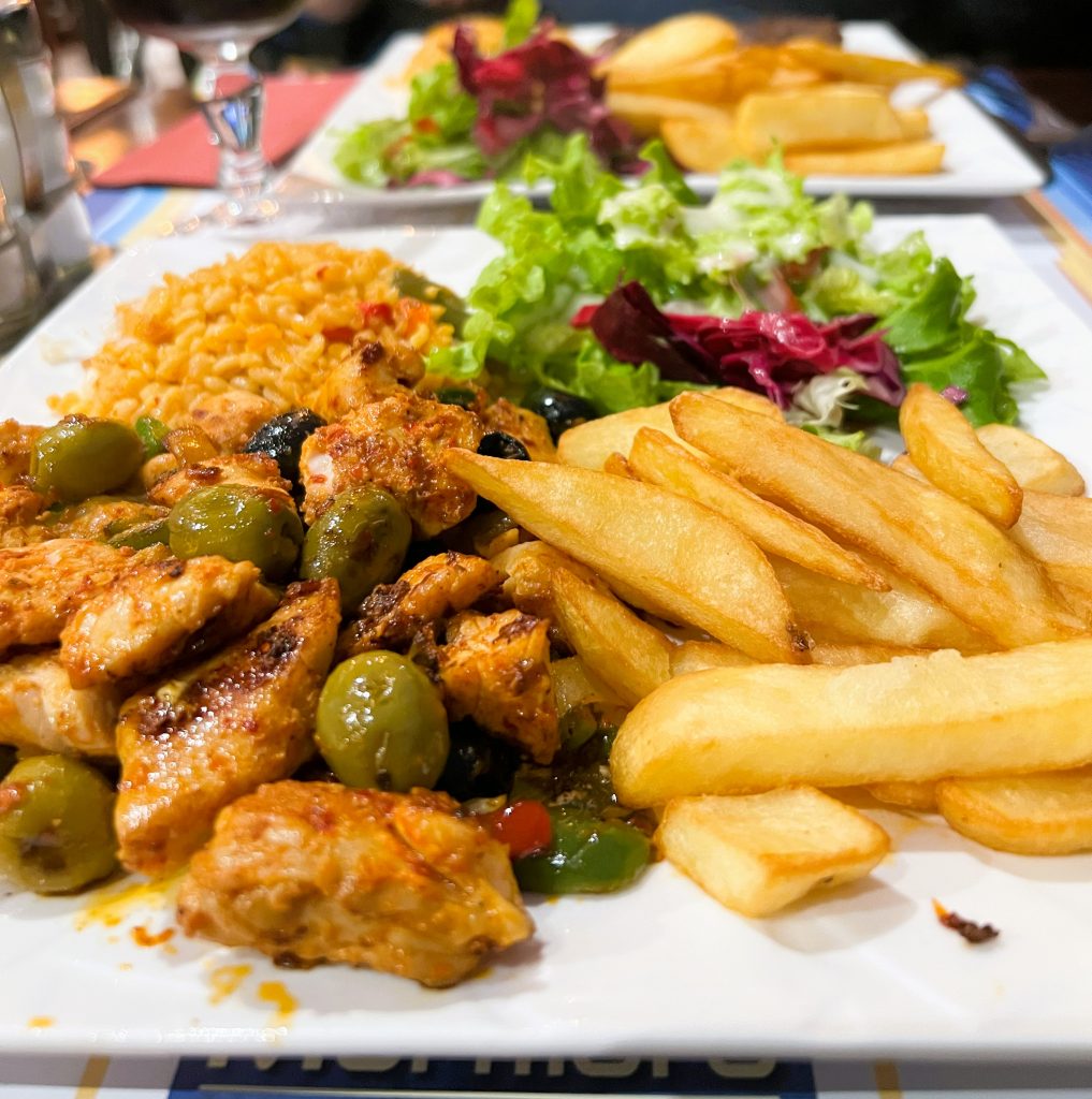 a plate filled with salad, pommes frites, and Turkish chicken with green olives