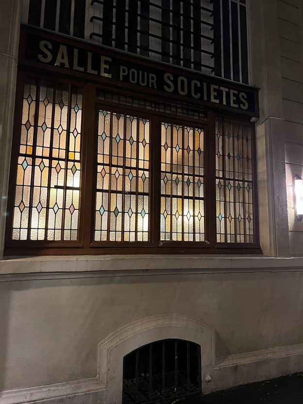 a night time photo of a stained glass window and a sign that says Salle pour Societies (Society Hall)